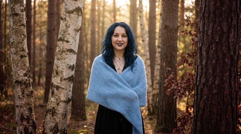 Madame Celestine smiling in a sky-blue shawl among birch and pine trees in low golden light, honoring the Finnish forest goddess Mielikki