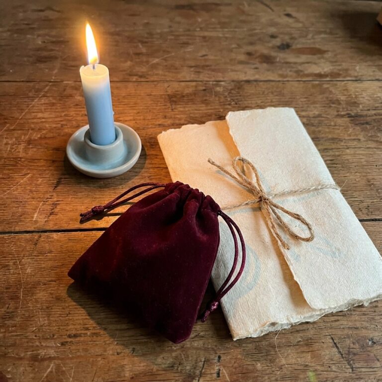 Folded handmade paper tied with twine, a lit light blue candle and a burgundy velvet bag on a wooden table, the simple tools used in healing spells